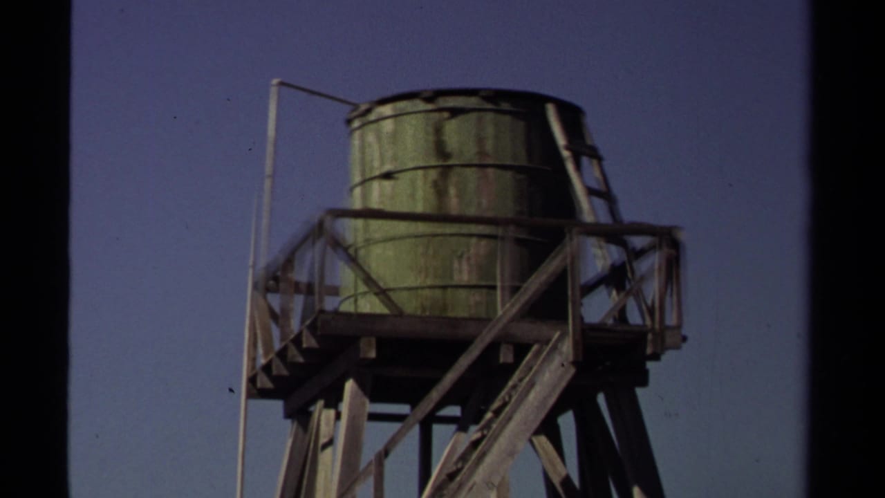1980 Mendocino 8mm frame showing a weathered green water tank elevated on a wooden support structure under clear sky.