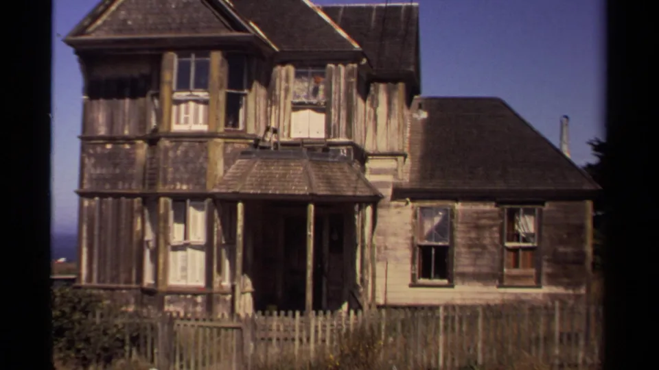 Weathered Victorian-style wooden house in Mendocino, California, seen under blue sky with porch, windows, and picket fence.