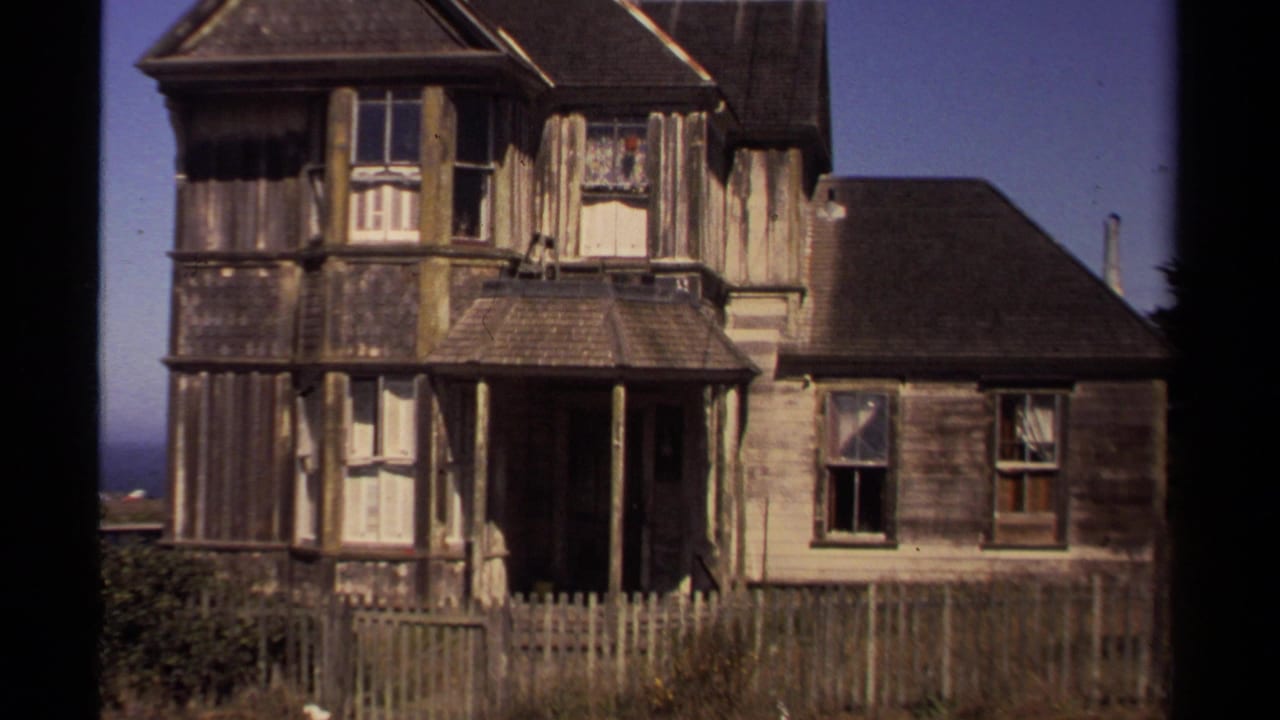 Old wooden house exterior with dark porch and fenced yard.