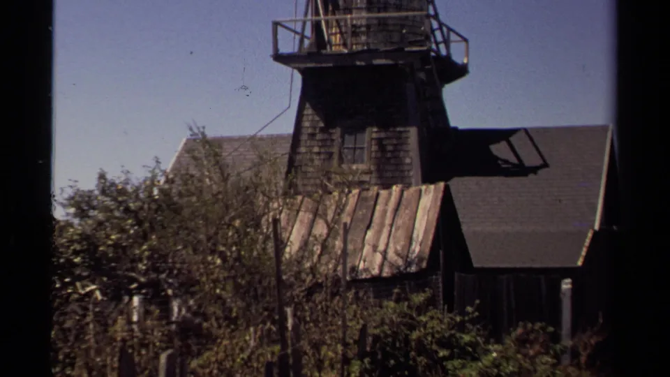 Weathered wooden upper structure in Mendocino, with railings, dark shingles, sloped roofs, shrubs, and open sky visible in the frame.