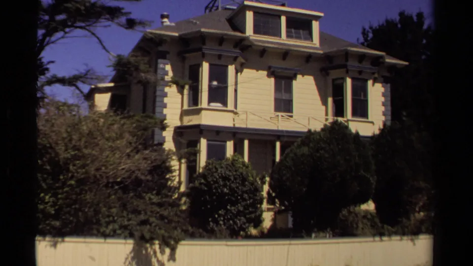 1980 Mendocino residential frame showing a two-story light-colored house with bay windows, porch, hedges, and trees.