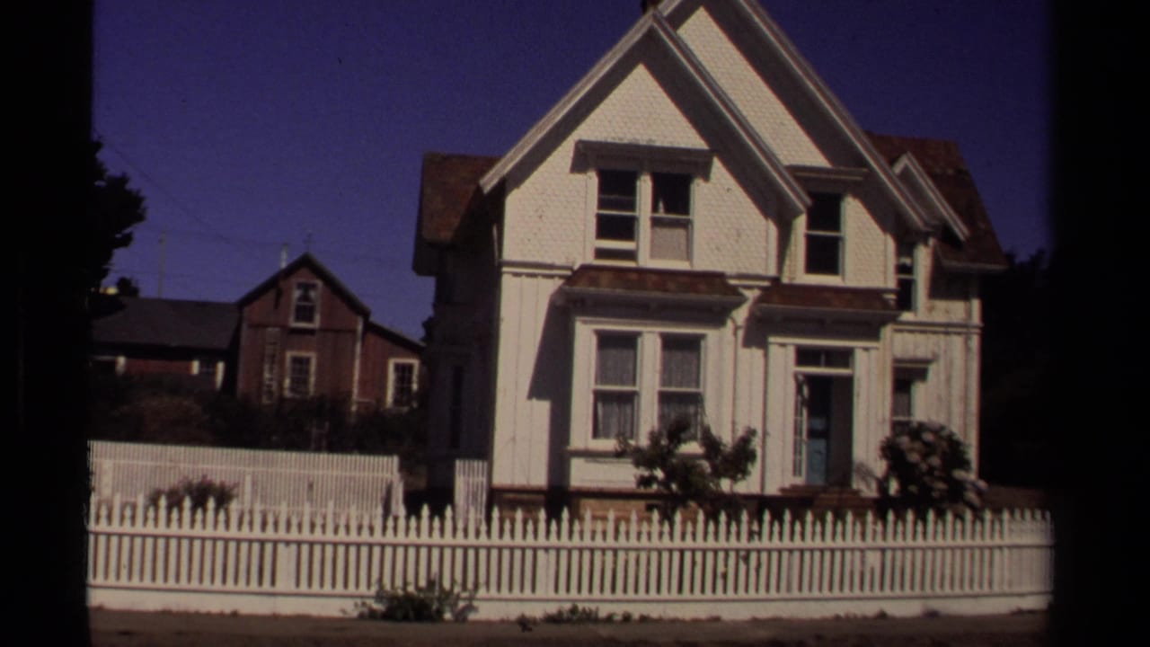 Mendocino, California residential exterior from 1980 with a white gabled house, picket fence, shrubs, and neighboring buildings.