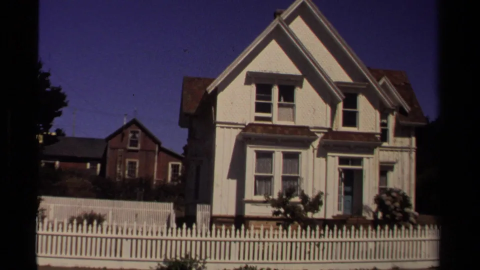 Mendocino residential exterior from 1980 showing a cropped white house front, picket fence, shrubs, and a darker neighboring house.