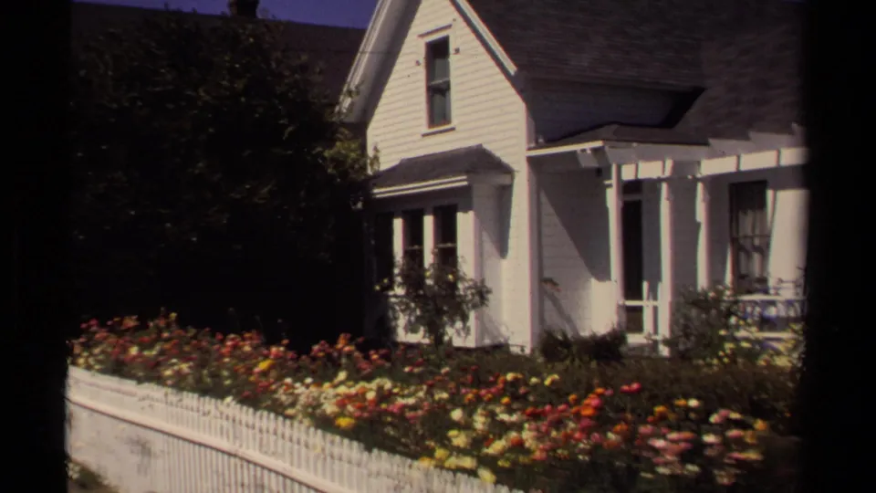 Final frame shows the Mendocino house exterior partly framed by darker shrubs, with flower beds and picket fence along the foreground.