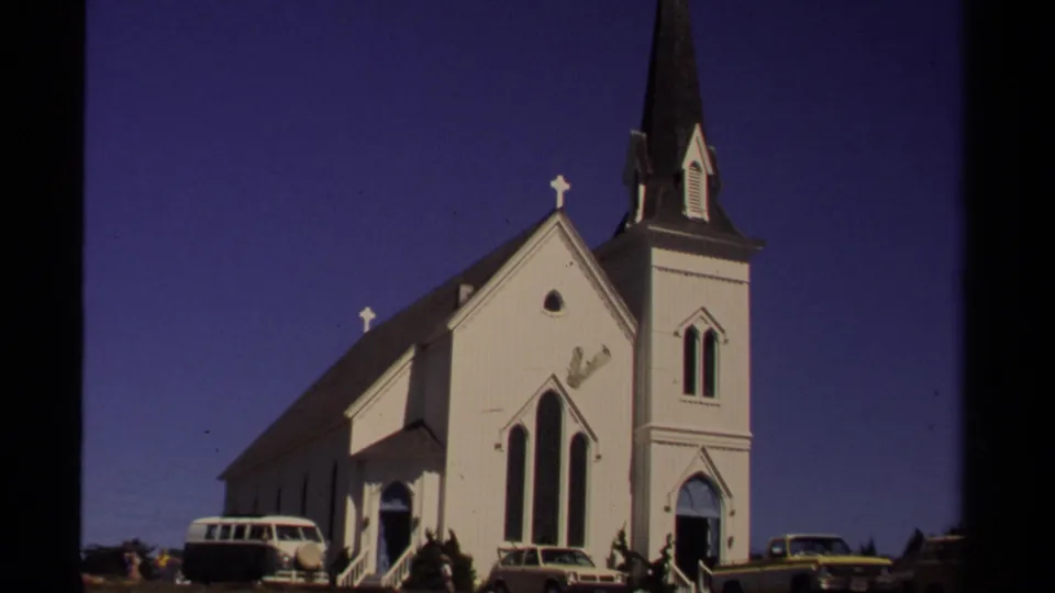 Mendocino, California 1980 home-movie view of a white church, dark steeple, crosses, and cars parked near the entrance.