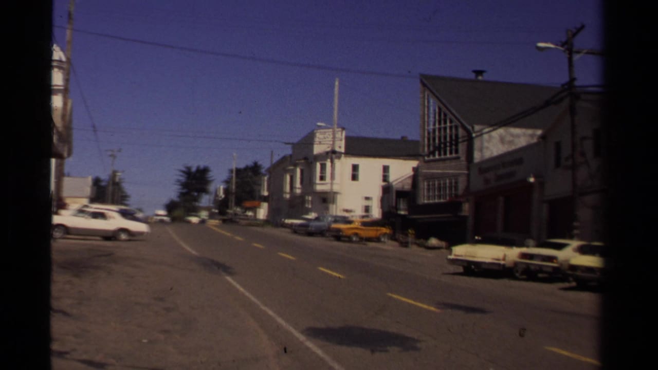 Mendocino street view with period cars along the curb, a yellow taxi, commercial buildings, utility lines, and bright midday light.