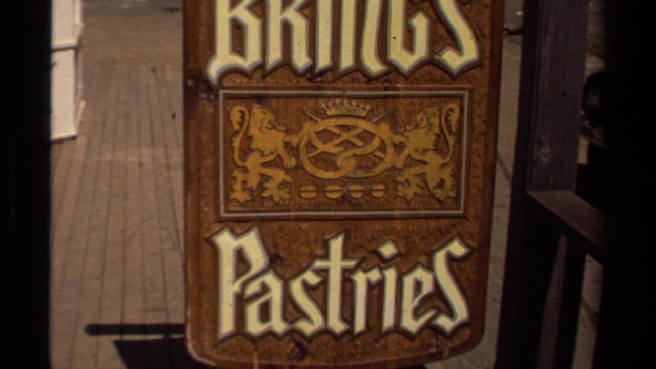 1980 Mendocino home-movie frame showing a wooden Kings Pastries sign with decorative lettering and lion motifs near a storefront.