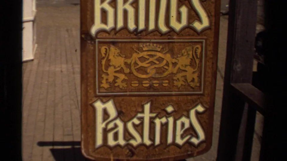 1980 Mendocino home-movie frame showing a wooden Kings Pastries sign with decorative lettering and lion motifs near a storefront.