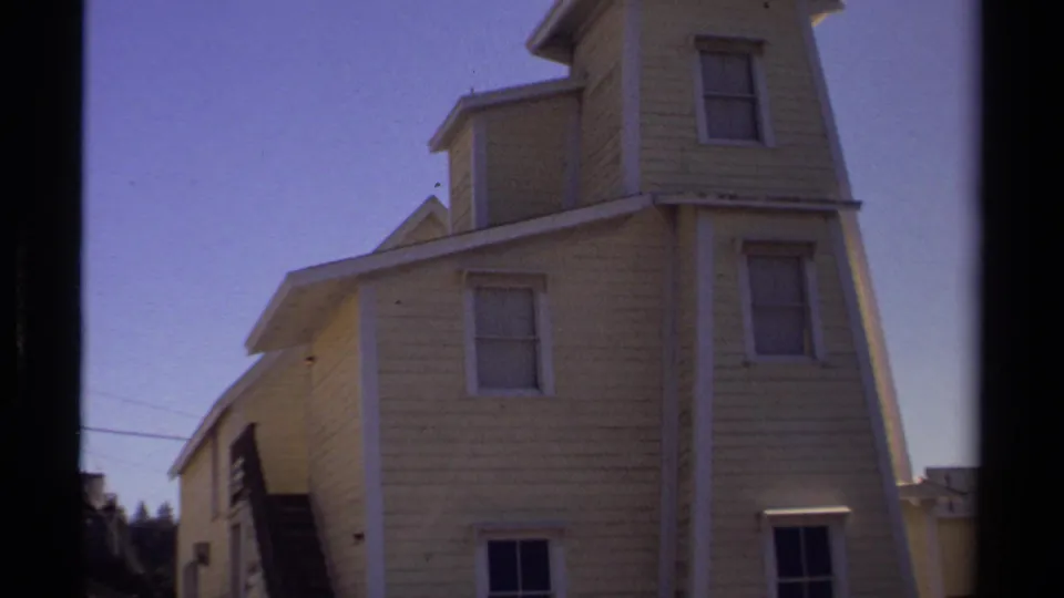 1980 Mendocino home-movie view of a yellow wood-shingled building with white trim, sash windows, and exterior stairs.