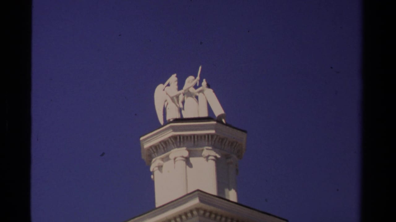 White classical figures on a rooftop pedestal against blue sky.