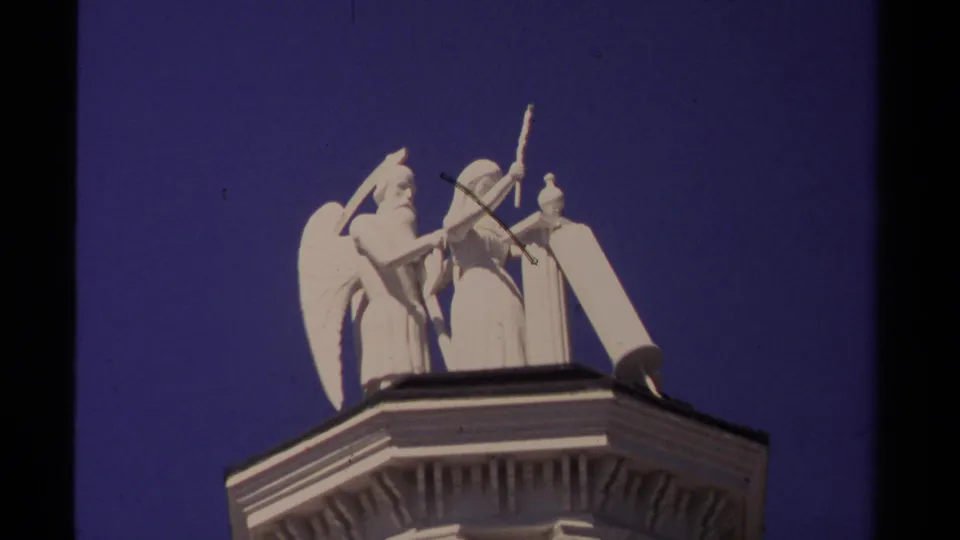 Rooftop angel sculpture with raised arm and wings, filmed in the Mendocino clip against a clear blue sky.