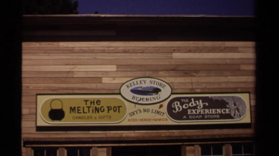A 1980-era Mendocino storefront frame shows weathered wood siding, the Kelley Store Building marker, and signs for several small shops.