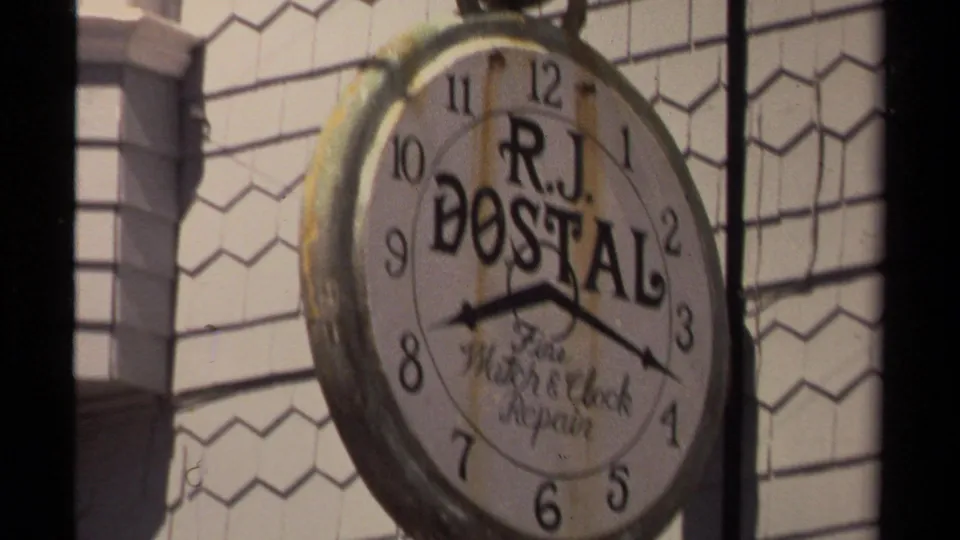 Close view of an R.J. Dostal Watch & Clock Repair clock-shaped sign on a Mendocino building exterior.