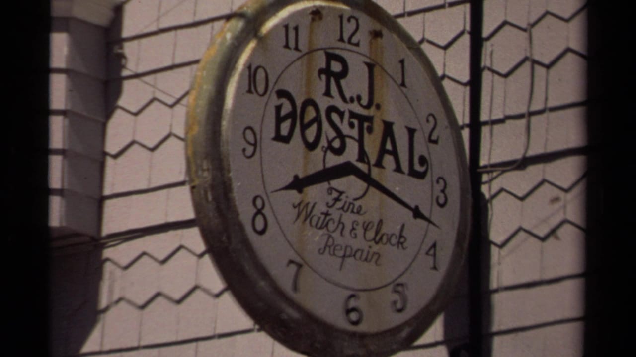 Large round R.J. Dostal clock repair sign on a shingled storefront.