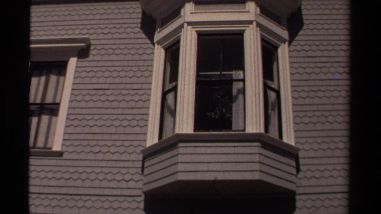 Mendocino storefront facade with gray shingles, a projecting bay window, and open-looking dark window panels in 1980 home-movie footage.