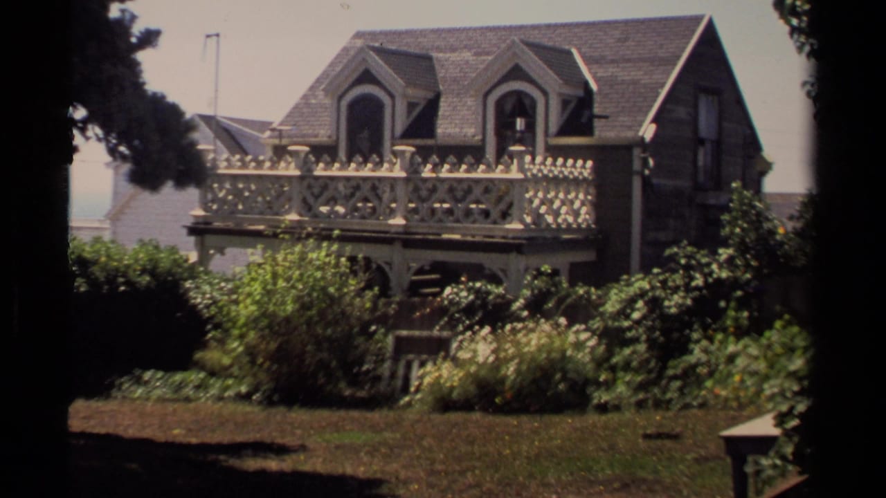 Victorian-style house with ornate balcony, dormer windows, and garden plantings.