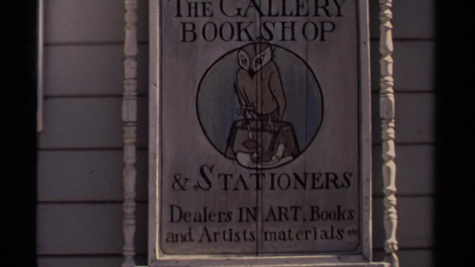 1980 Mendocino footage frame showing The Gallery Bookshop and Stationers sign with owl artwork and art-supplies text on a wooden storefront.