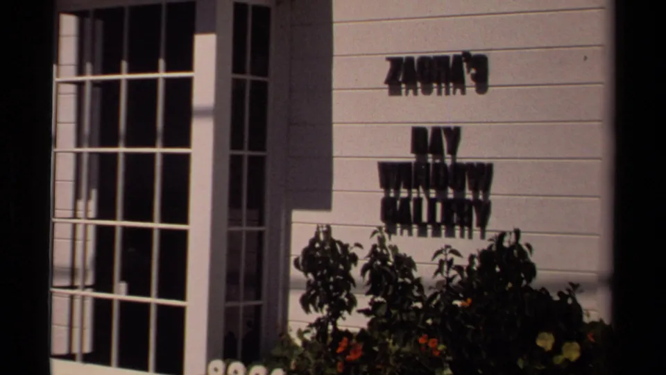 Mendocino storefront detail showing a Simon's Place wall sign above shrubs and flowers beside tall windows.