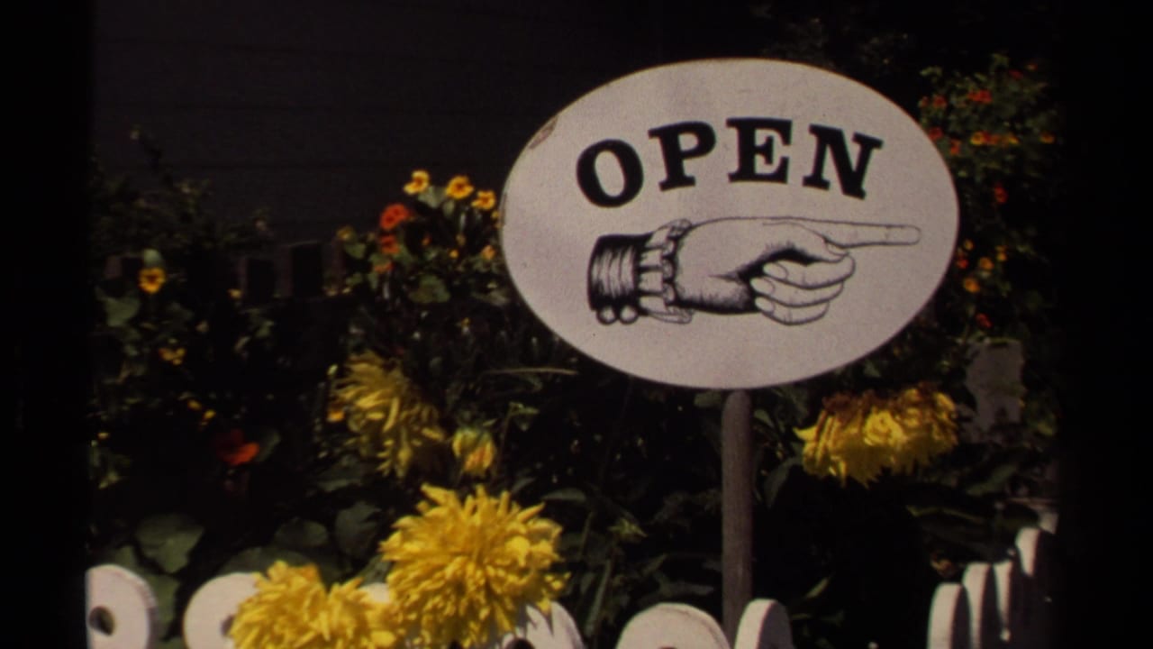 Oval OPEN sign with a pointing hand among yellow flowers and foliage.