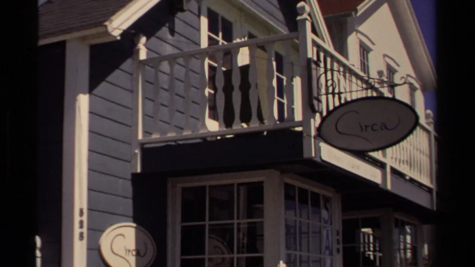 A Mendocino storefront with white balcony railing and oval shop signs appears in bright 1980 home-movie footage.