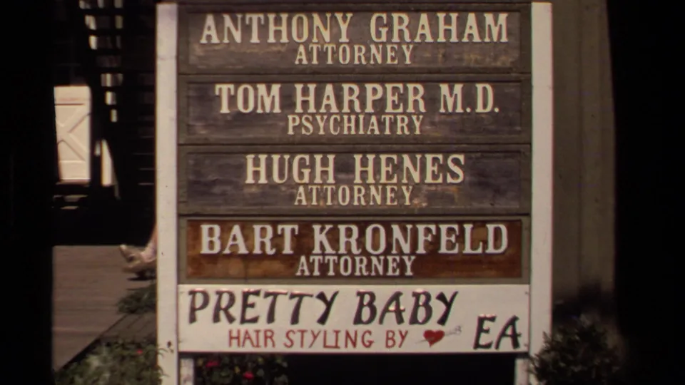 Close view of a Mendocino business directory with attorney, psychiatry, and hair-styling signage visible in 1980 home-movie footage.