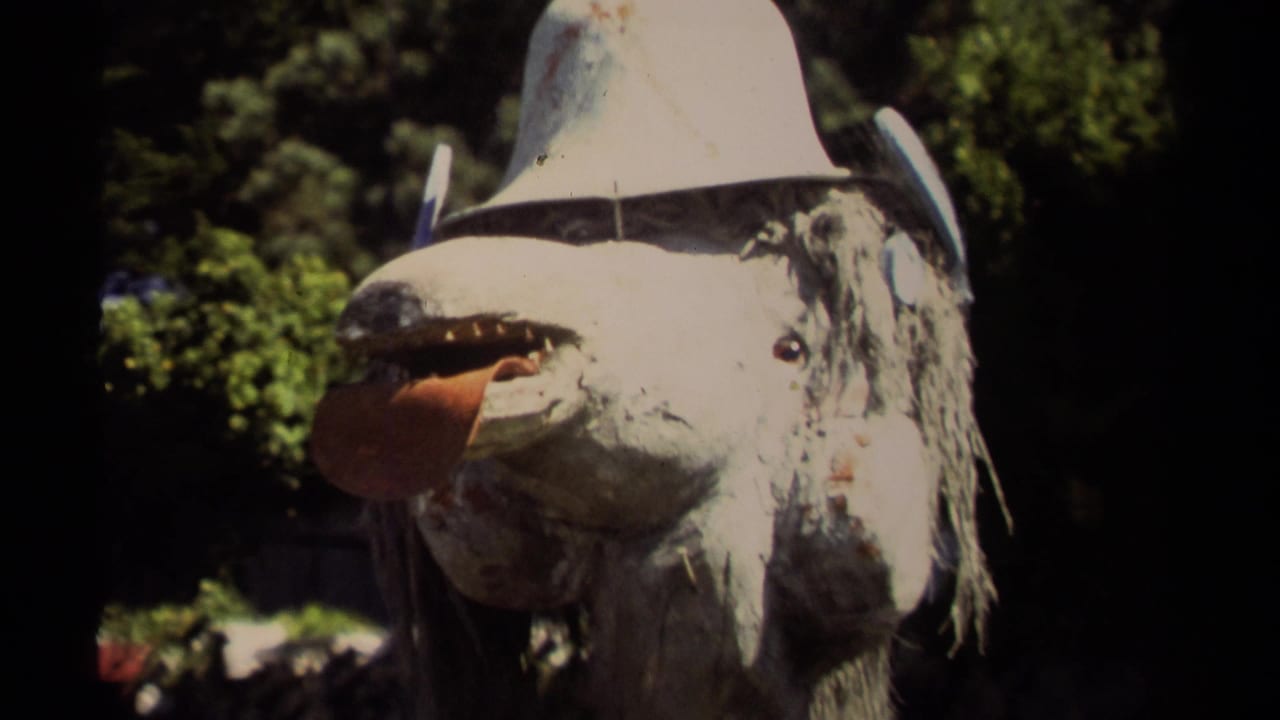 1980 8mm frame from Mendocino showing a weathered goat-like mask on a pole, wearing a white hat with foliage behind it.