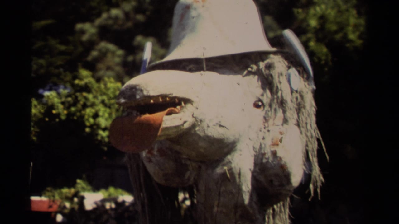 Weathered animal mask with tongue extended, white hat, and trees in the background.