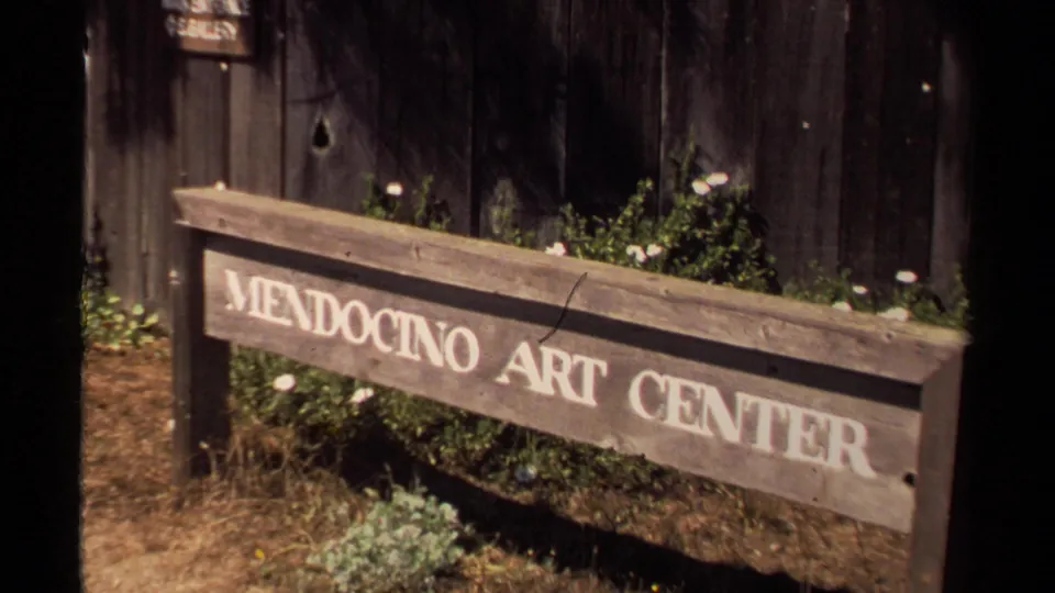 Wooden Mendocino Art Center sign outside a rustic building in 1980 Mendocino home-movie footage.