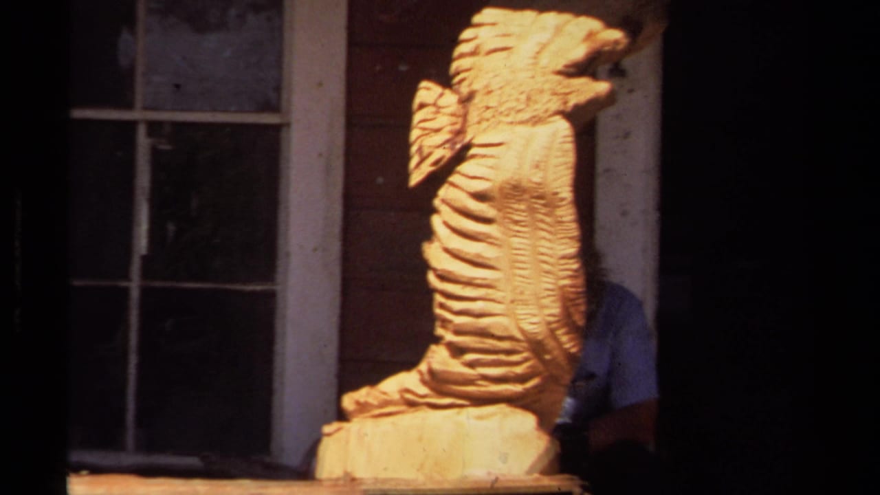 Closer view of the carved wooden creature with a person partly hidden behind it.