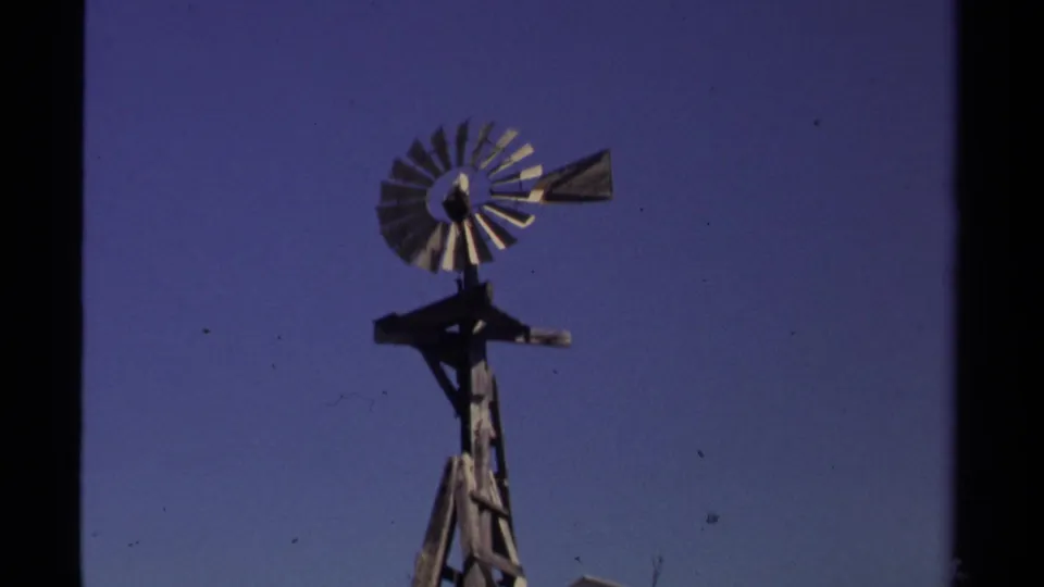 Mendocino-area 8mm frame showing a metal windmill tower and wheel silhouetted against a deep blue sky.