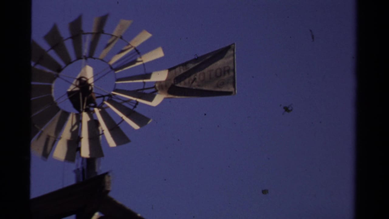 Closer 8mm view of a windmill in Mendocino, with a weathered tail vane showing partially readable lettering against the sky.