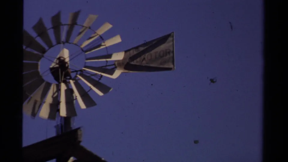 Closer 8mm view of a windmill in Mendocino, with a weathered tail vane showing partially readable lettering against the sky.