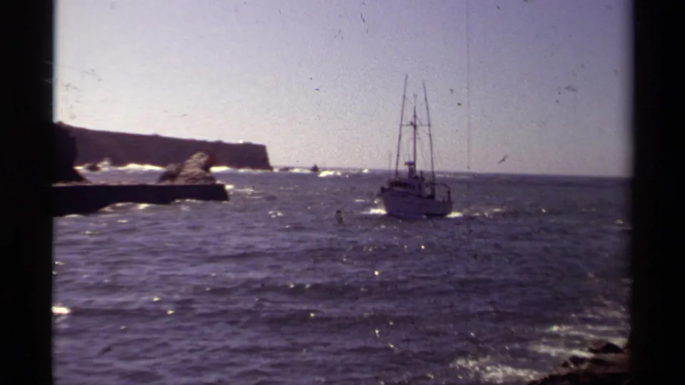 1980 Mendocino coastal footage shows a small offshore boat crossing sunlit water near rocky cliffs and a low headland.