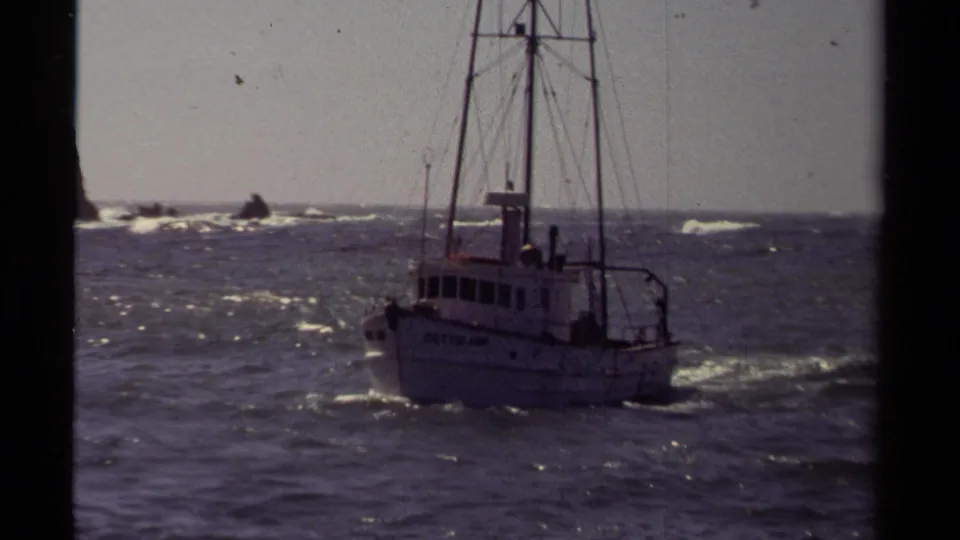 A closer 8mm frame shows the white DUTCH LADY boat riding through choppy Mendocino coastal water under a pale sky.