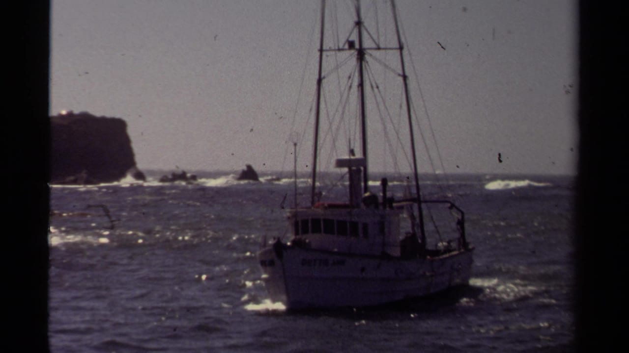 A small fishing boat moves through choppy Mendocino coastal water in 1980, with a rocky headland and surf behind it.