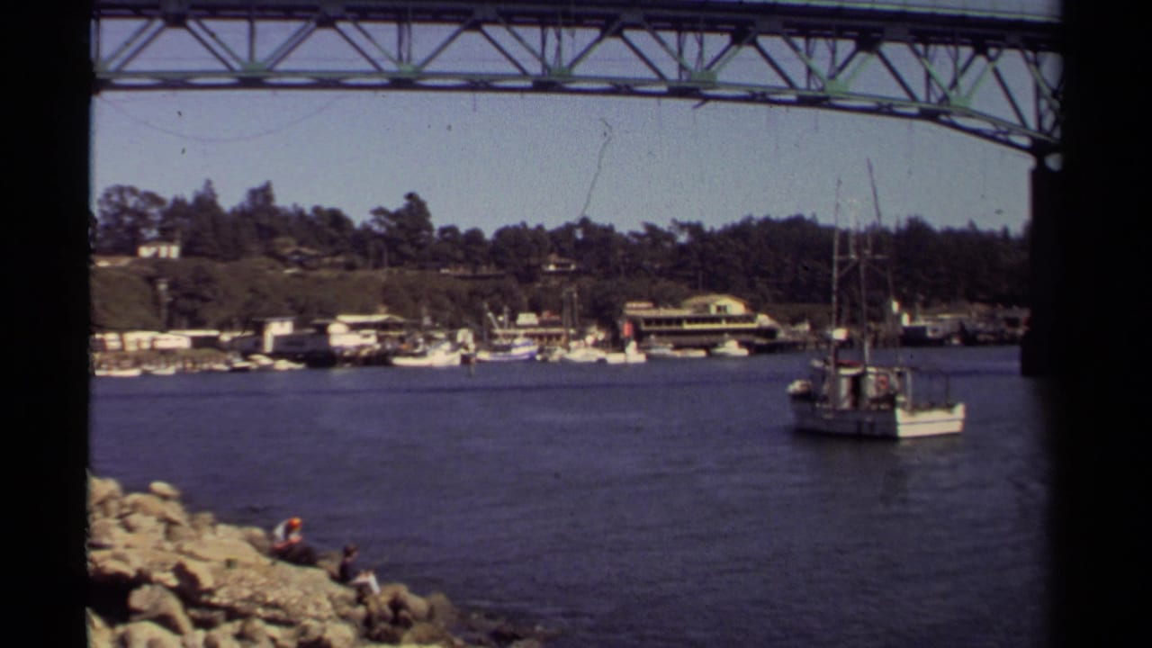 1980 8mm view of a small white boat on the Noyo River near the Lt. Charles L. Larson Memorial Bridge in Mendocino, California.