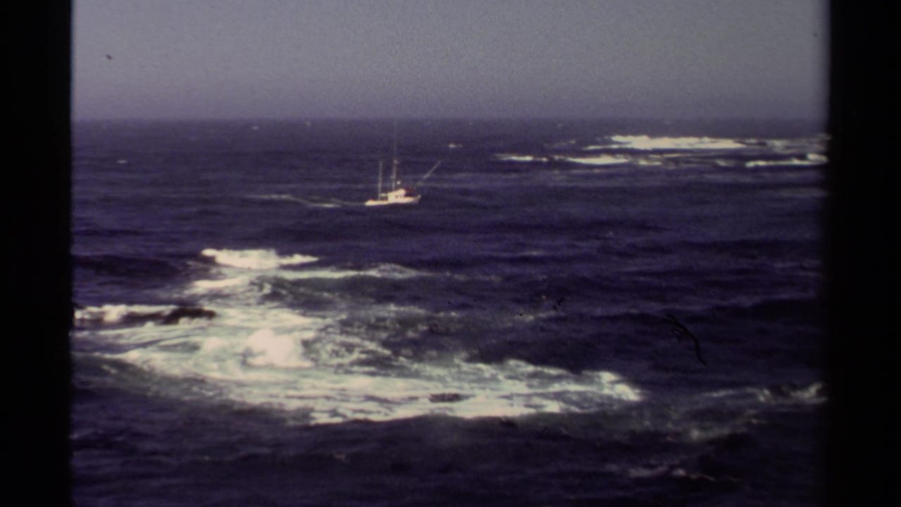 Mendocino coastal home-movie frame with a small fishing boat beyond foamy surf and choppy Pacific water.