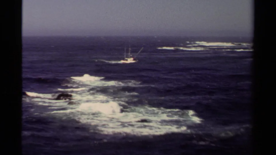 Vintage 8mm coastal frame showing a small white vessel past rough surf along the Mendocino shoreline area.