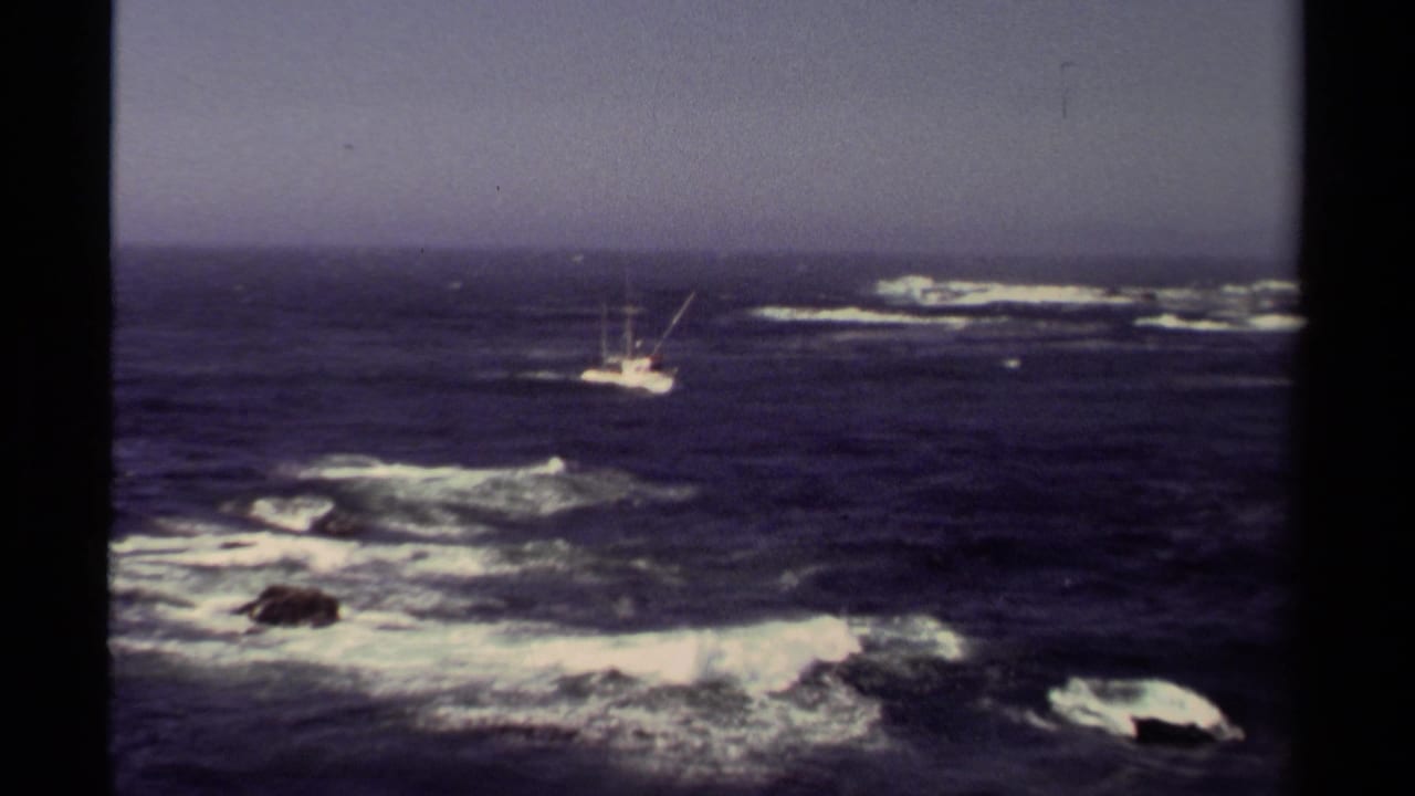 Fishing boat on open water with white surf over distant rocks.