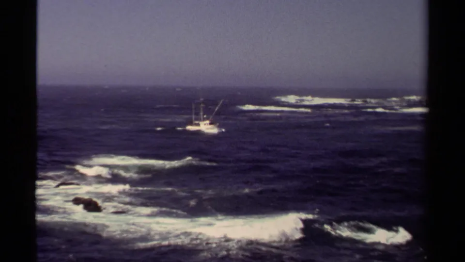 8mm coastal frame showing a small white boat beyond rolling waves and dark rocks along the Mendocino shoreline.