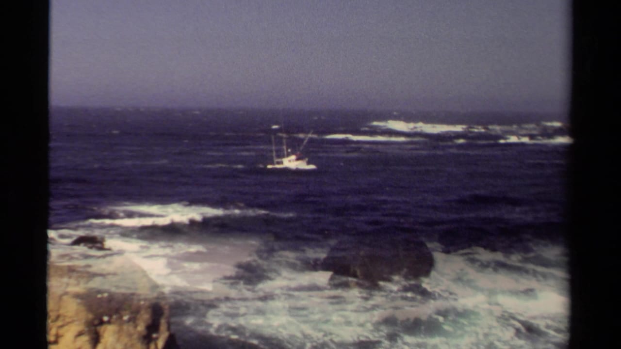1980 Mendocino 8mm frame showing a small fishing boat beyond white surf breaking around coastal rocks.