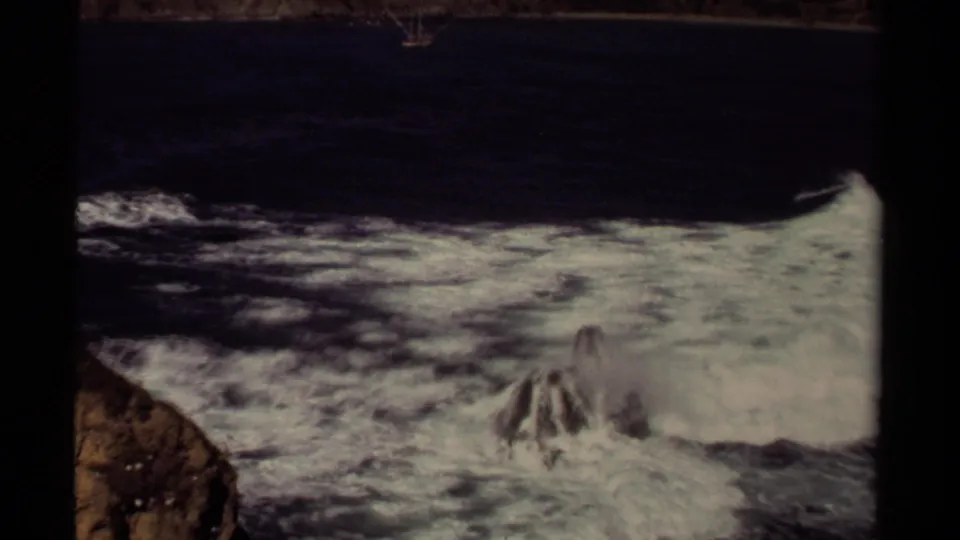 1980 Mendocino coastal frame with turbulent white foam washing across rocks after a breaking wave.