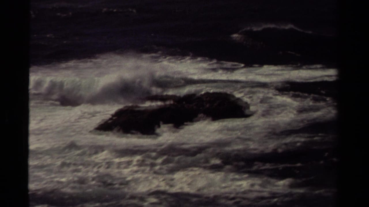 Rough ocean waves breaking around dark rocks near shore.
