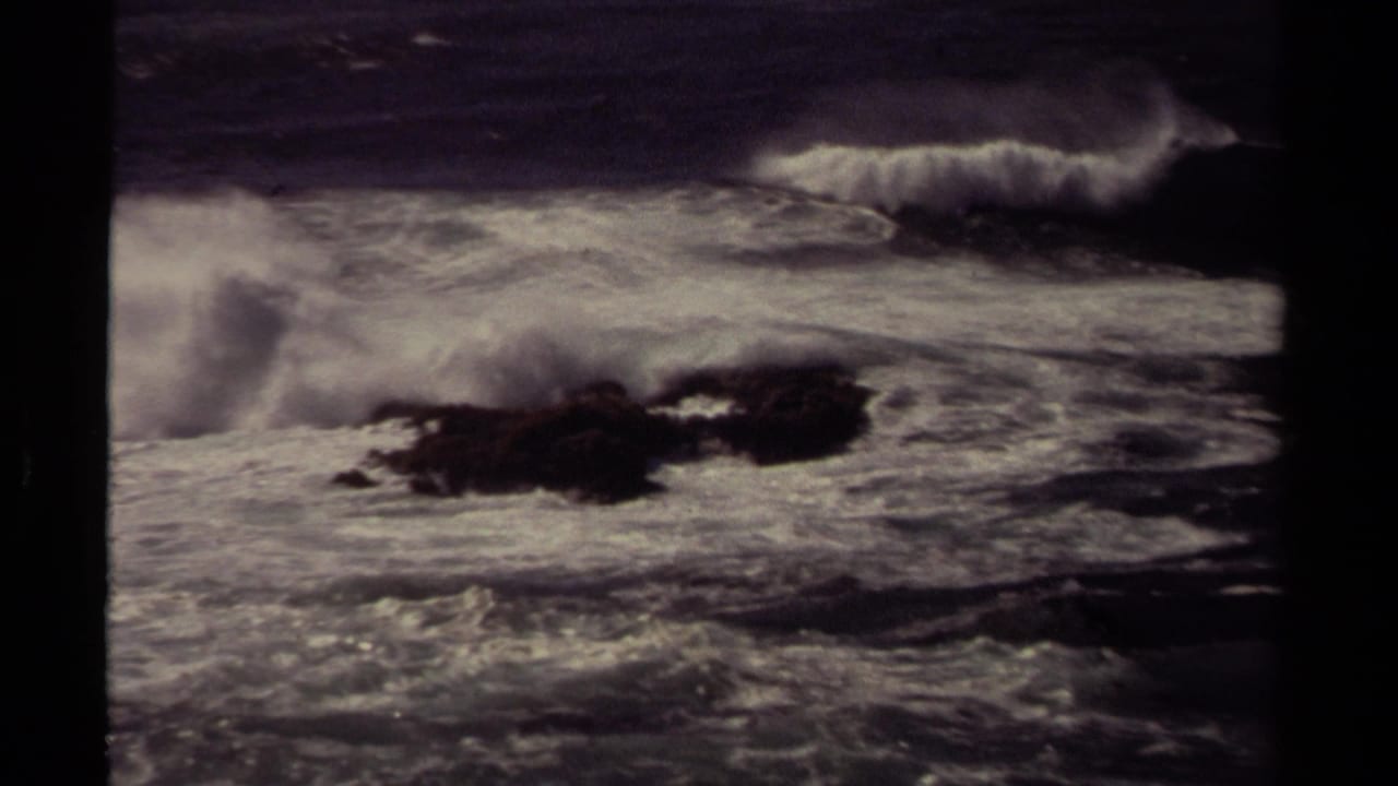 1980 Mendocino shoreline frame with a cresting wave, white spray, and dark rocks in rough Pacific water.