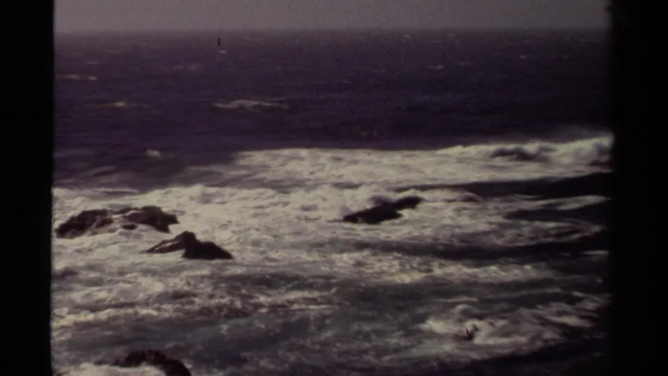 Wide 1980 Mendocino coast frame showing rough surf, scattered dark rocks, open water, and a hazy horizon.