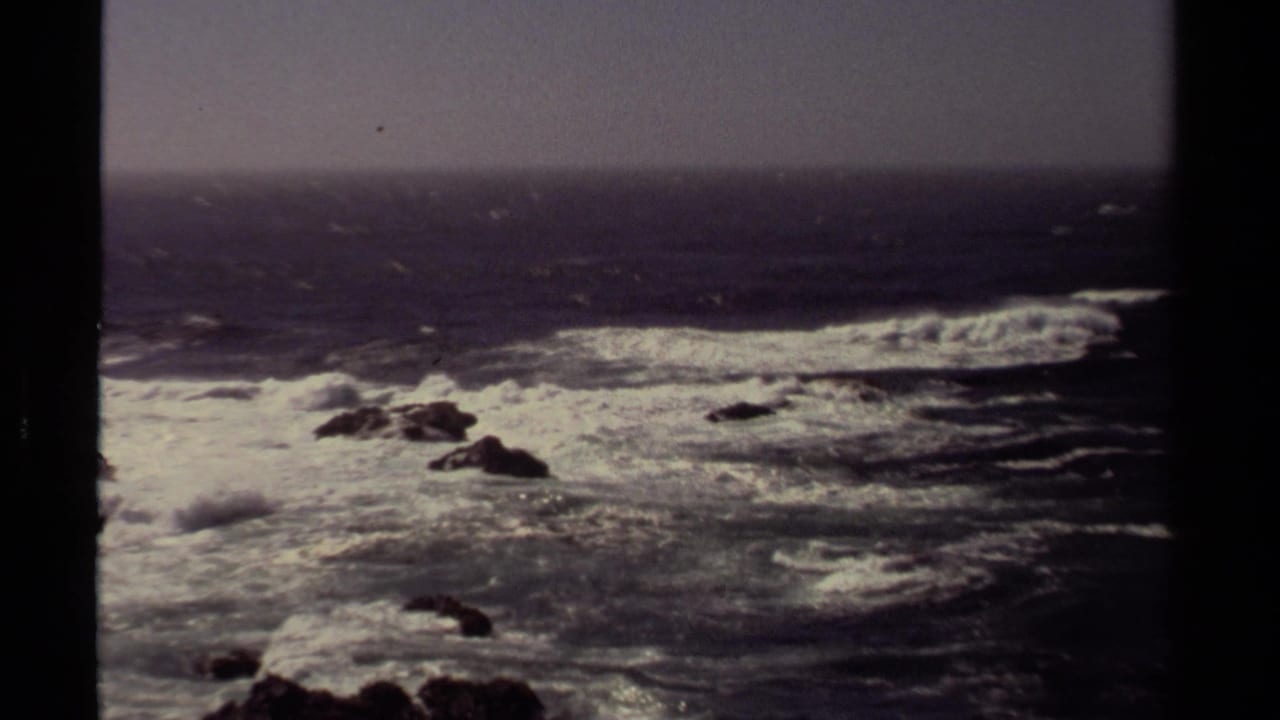 1980 8mm home-movie view of turbulent Mendocino surf and offshore rocks seen through a dark structural frame.