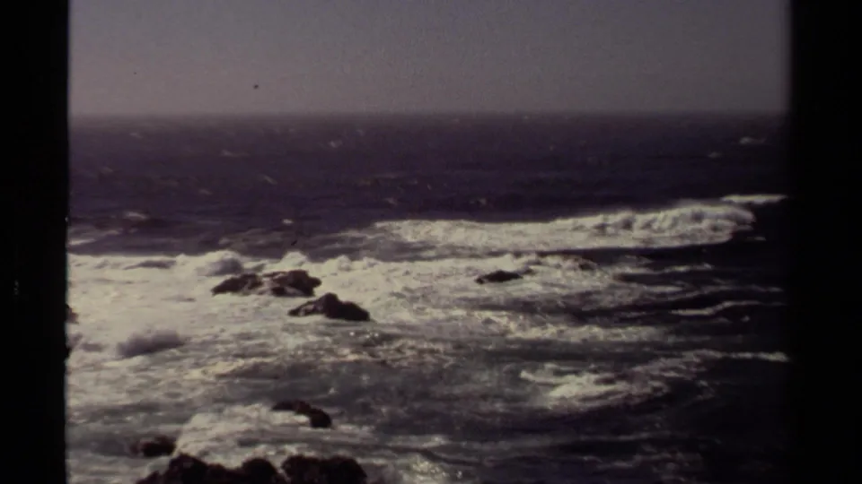 1980 8mm home-movie view of turbulent Mendocino surf and offshore rocks seen through a dark structural frame.
