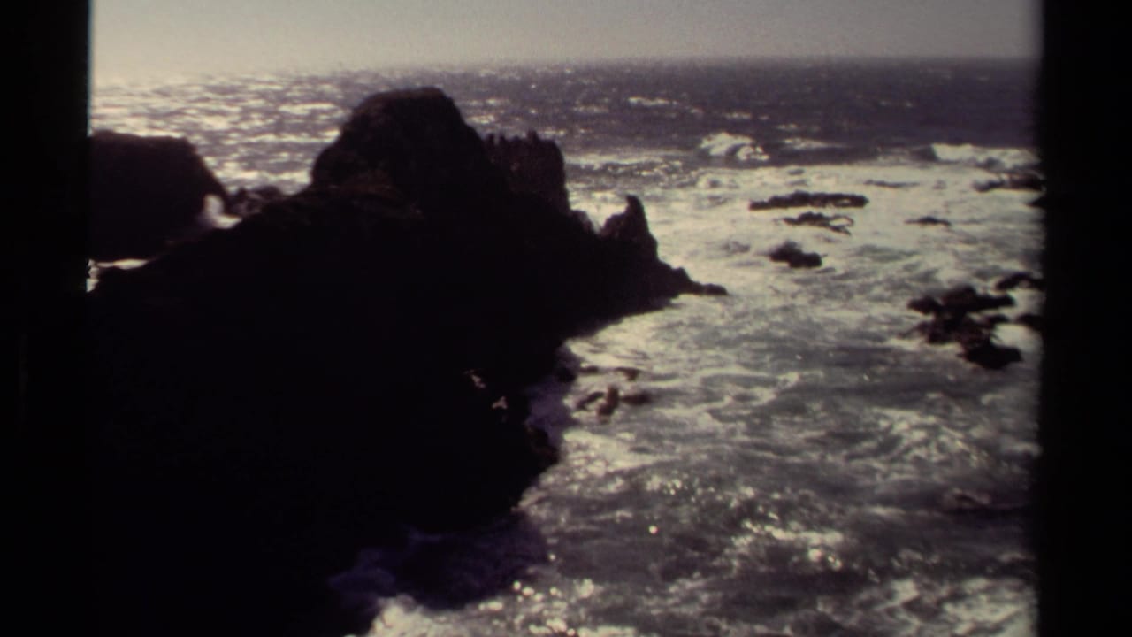 1980 8mm home-movie view of the Mendocino coast with dark rocks, bright surf, and hazy ocean light.