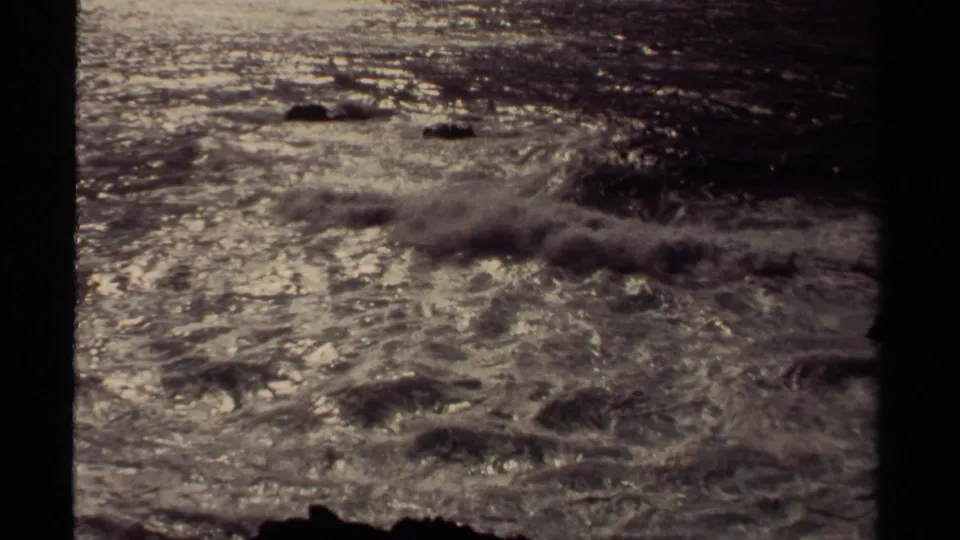 Mendocino coastal surf churns across dark rocks, with bright reflections and softened 8mm film texture.