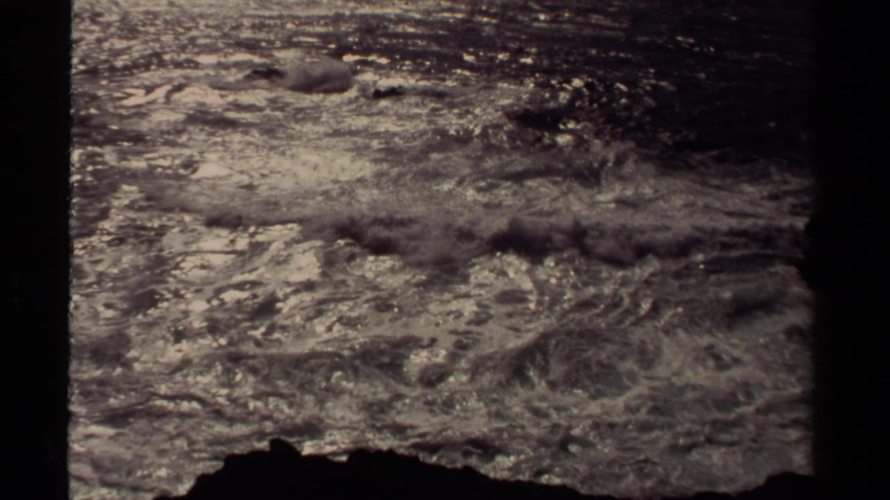 1980 8mm home-movie view of waves breaking near dark rocks on the Mendocino shoreline, with sun glinting on the water.
